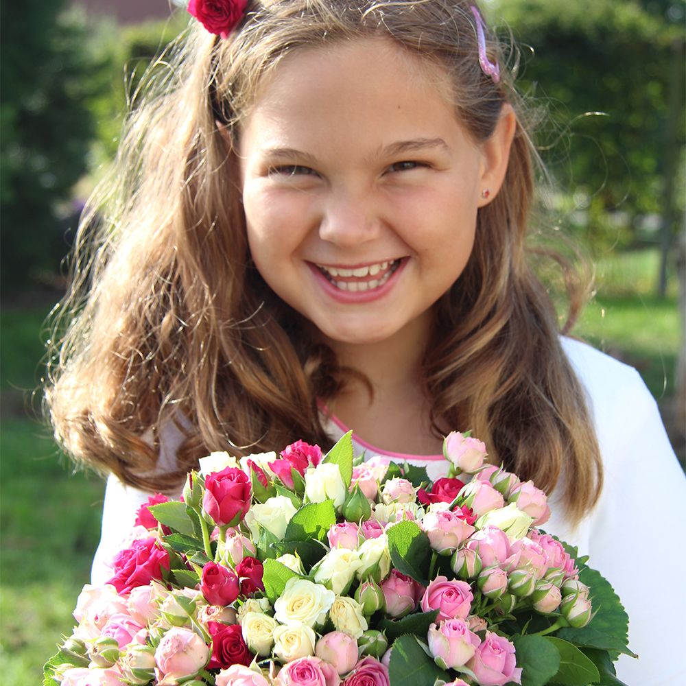 Ein lächelndes Mädchen mit gewelltem braunem Haar hält einen leuchtenden Strauß rosa und weißer Rosen in der Hand